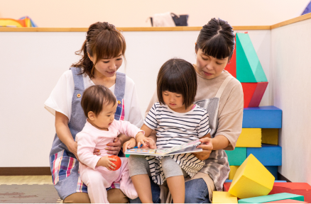 室内で子どもが周囲に見守られながら遊んでいる様子の写真