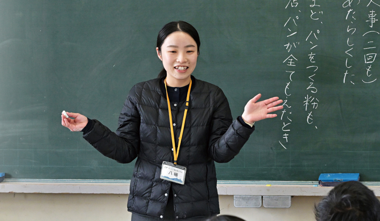 教室で黒板の前に立って説明が行われている様子の写真