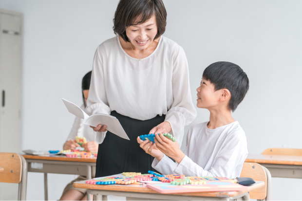 教室で子どもが机に置いた教材を使いながらやり取りをしている様子の写真