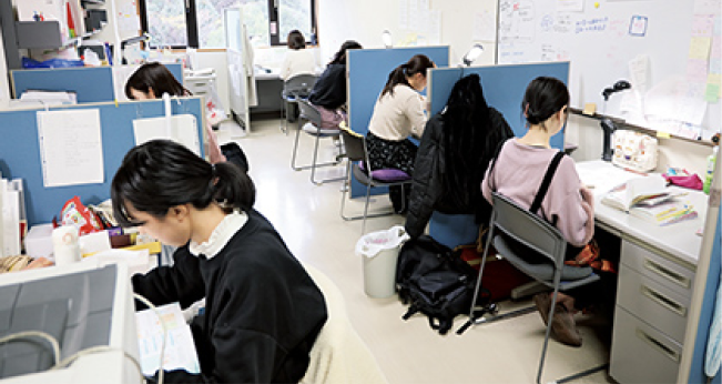 仕切りのある机で複数の人が作業や学習に取り組んでいる様子の写真