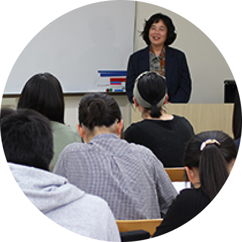 教室で前方から講義が行われ、受講者が席についている様子の写真