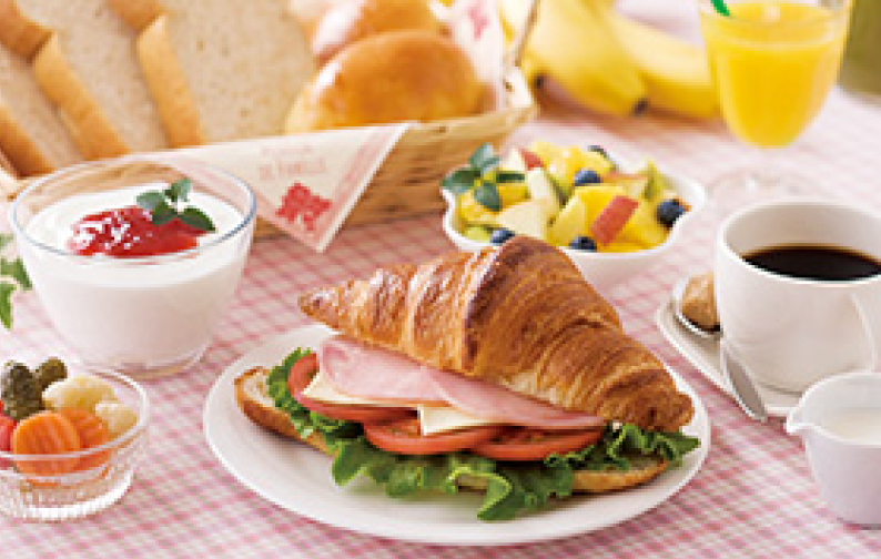 クロワッサンサンドやフルーツ、ヨーグルトなどが並んだ洋朝食の写真