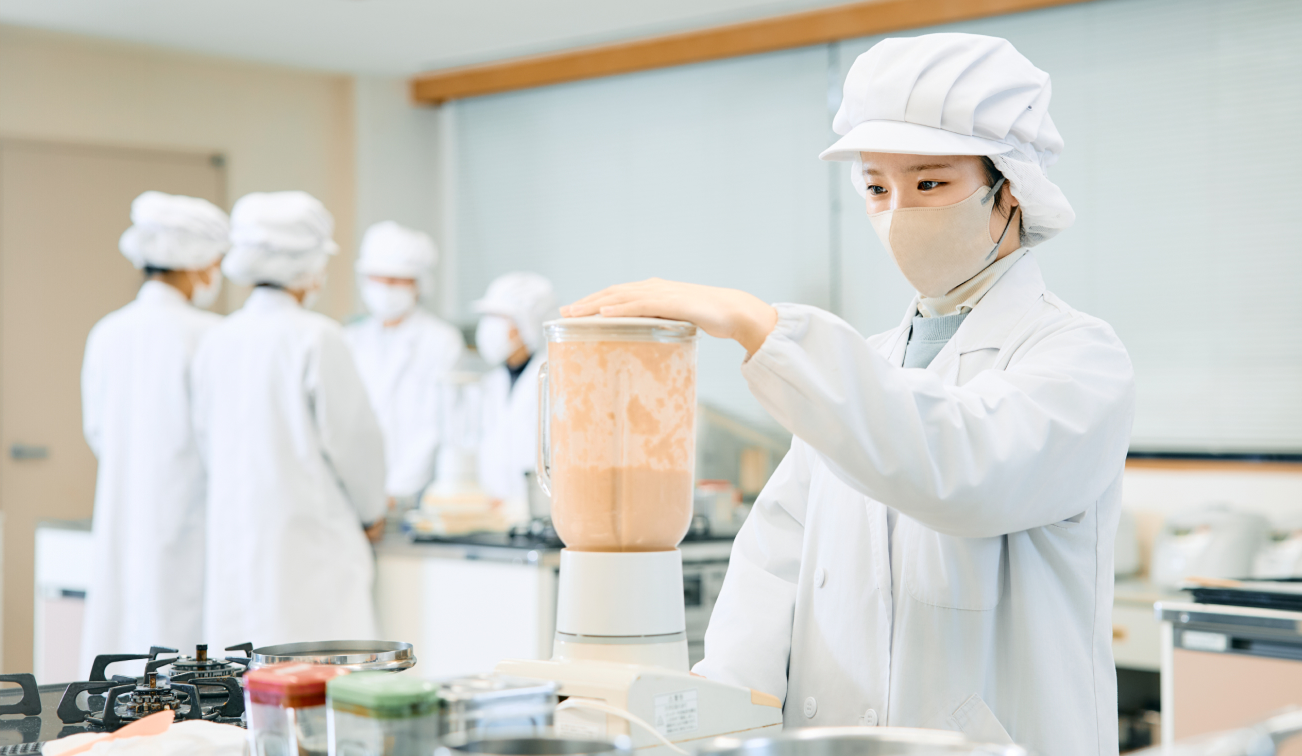 厨房で白衣を着た人がミキサーを操作して調理作業をしている様子の写真
