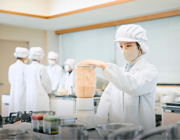 厨房で白衣を着た人がミキサーを操作して調理作業をしている様子の写真