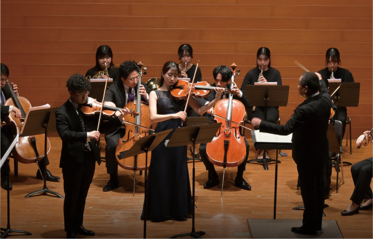 ステージ上で指揮者のもと演奏が行われている様子の写真